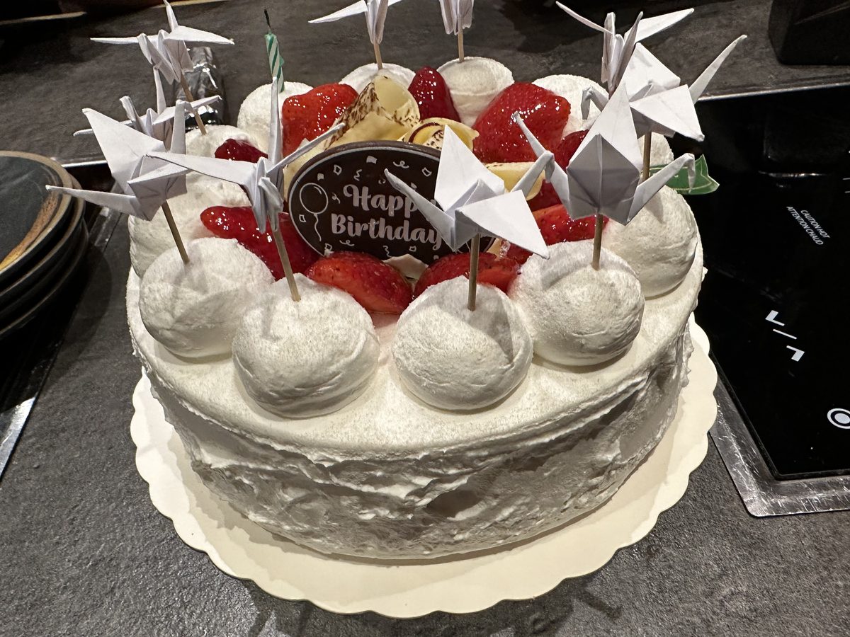 Overhead view of the Japanese birthday cake — white cream cake with strawberries and origami cranes on top