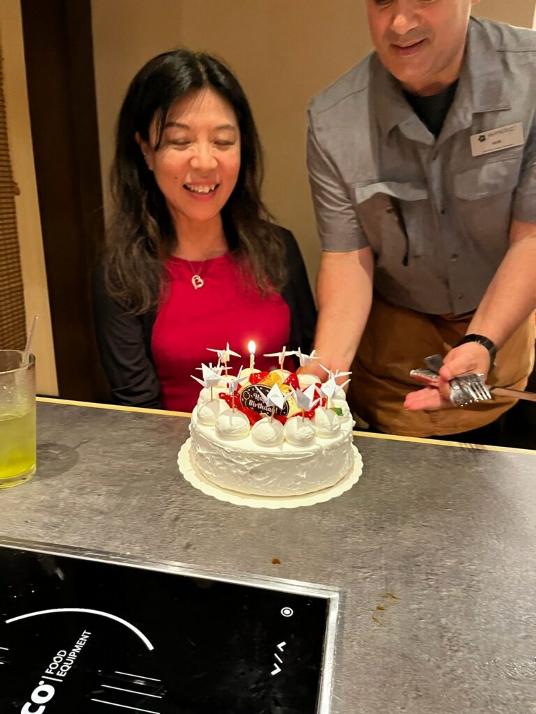 Ako smiling as a Hanagi staff member presents a Japanese birthday cake decorated with origami cranes