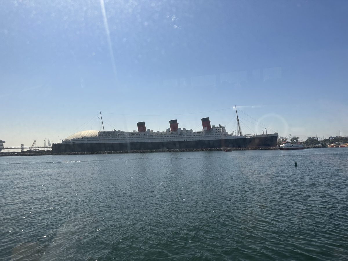 The Queen Mary seen from the Catalina ferry — all three funnels visible as the ship recedes across Long Beach harbor