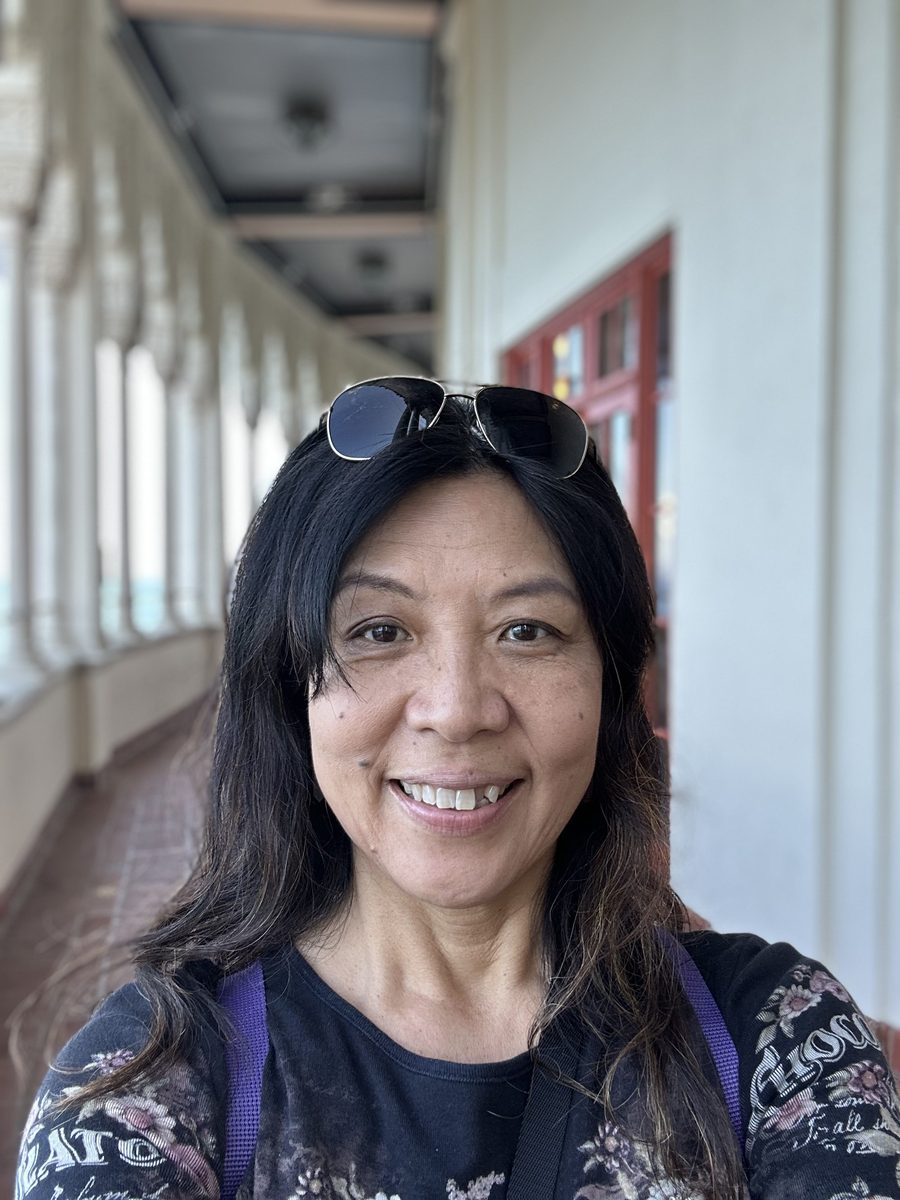 Ako smiling in the Avalon Casino's white arched colonnade, sunglasses on her head, ocean visible through the arches behind her
