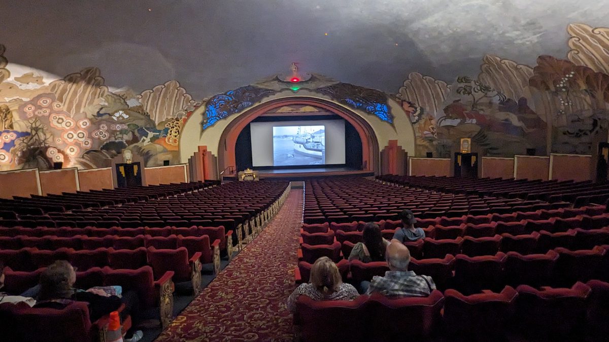 Inside the Avalon Casino Theatre — Art Deco ceiling murals of sea creatures over red velvet seats, a black-and-white film on screen