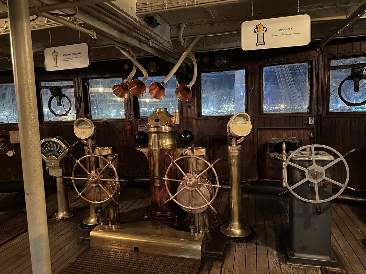 The Queen Mary's wheelhouse — original brass steering wheels, binnacle compass, and navigation instruments in the dark wood bridge