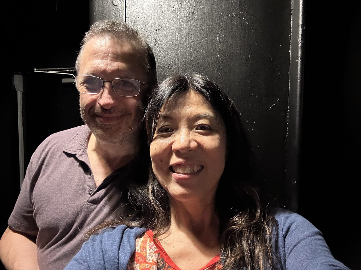 Eddy and Ako smiling together in a dark interior space against a large black painted bulkhead door