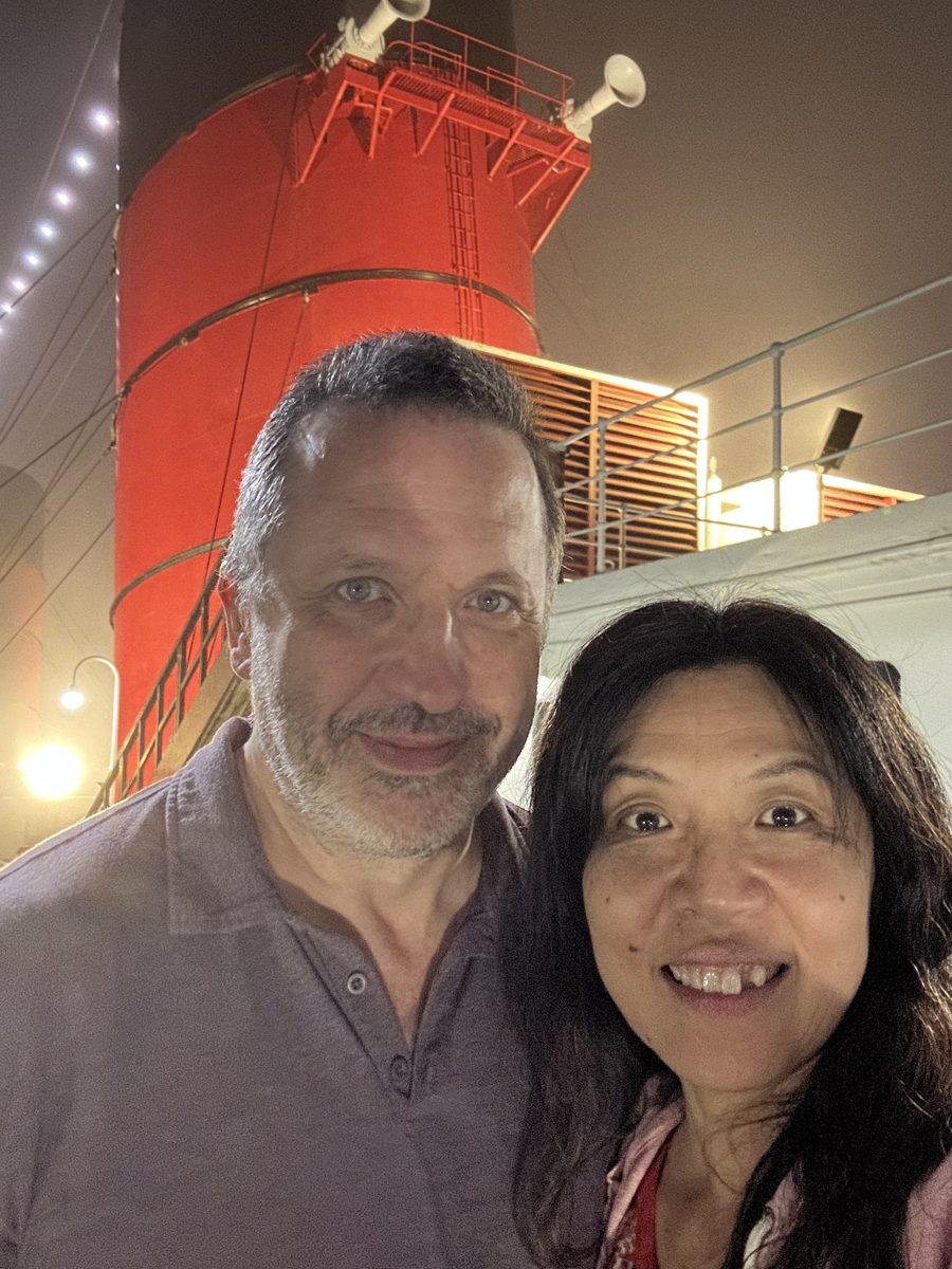 Eddy and Ako selfie at night on the Queen Mary deck, the red funnel glowing behind them in the fog