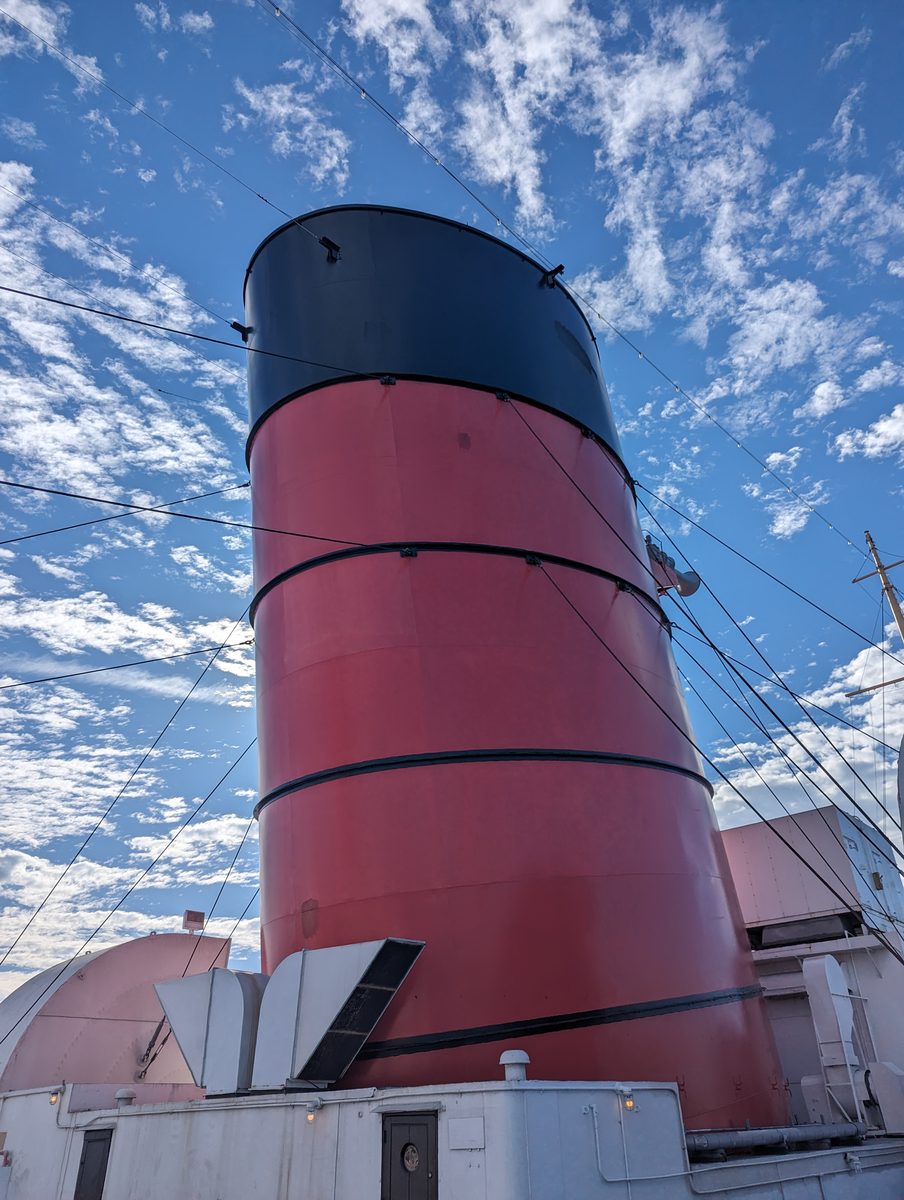 The Queen Mary's iconic red and black funnel towering against a blue sky