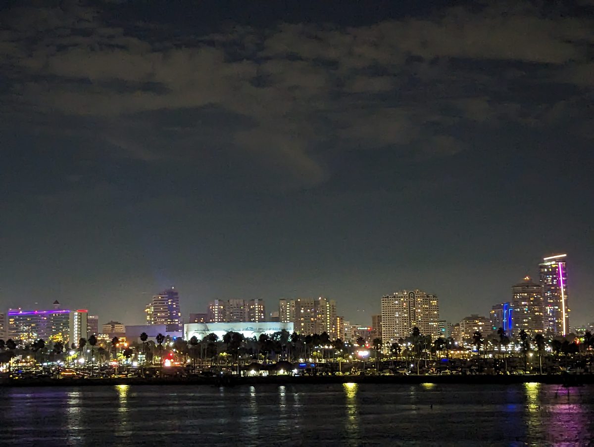 Long Beach skyline at night from the Queen Mary — palm trees, the Long Beach Arena, and colorful city lights reflected in the harbor