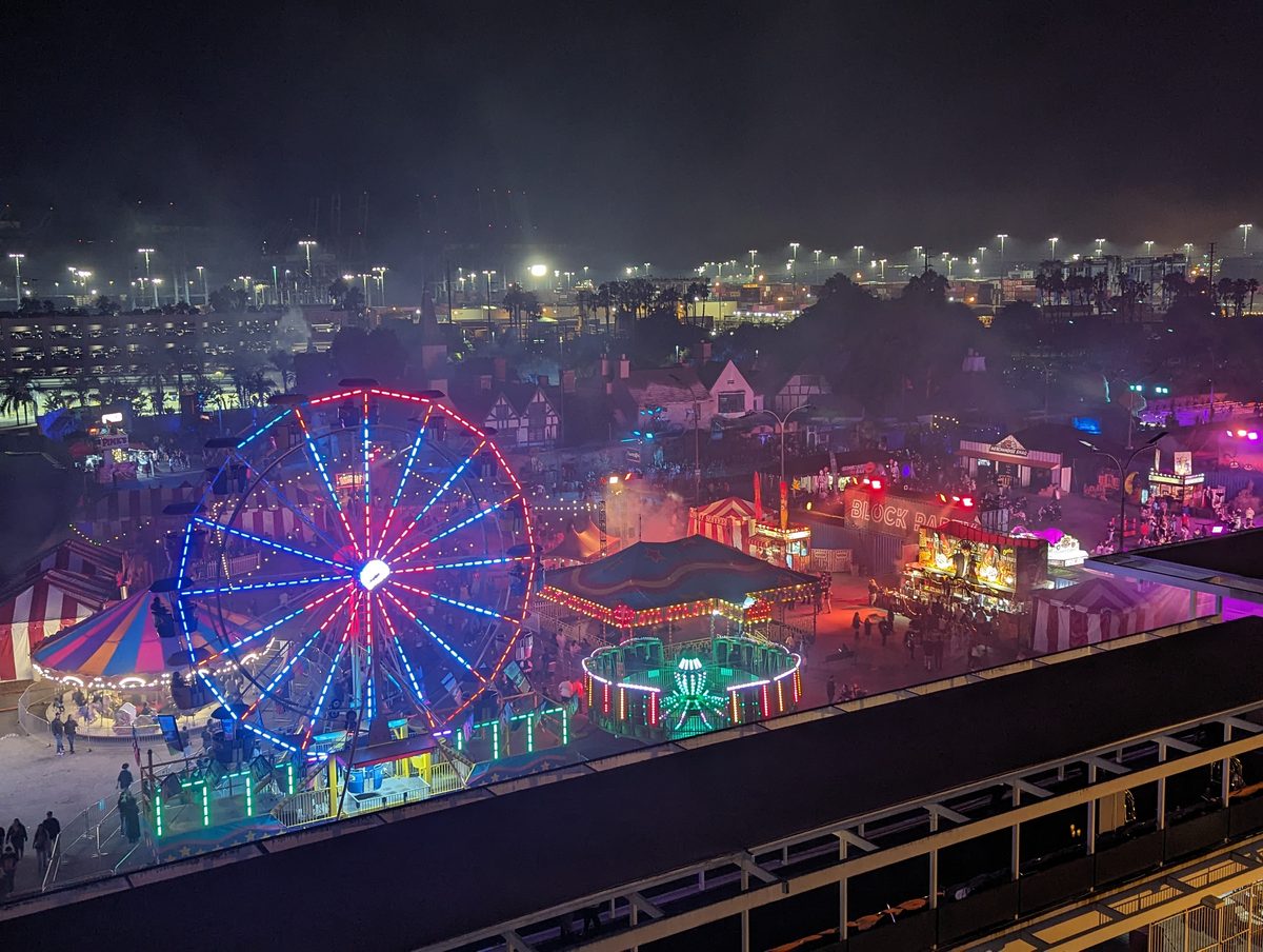 The Queen Mary Scream Zone Halloween carnival at night — a glowing Ferris wheel with red and blue LEDs, carnival tents and rides below