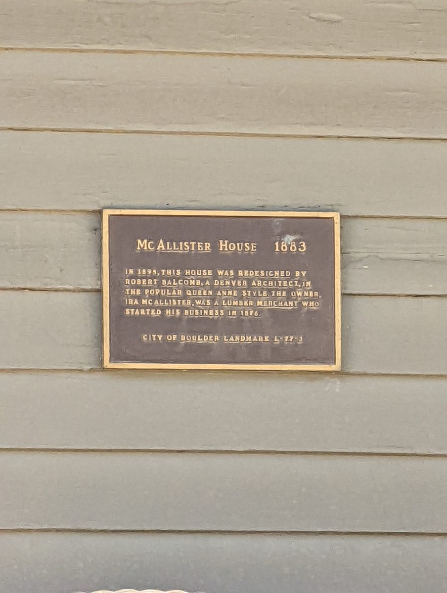 A close-up of the bronze historic landmark plaque reading McAllister House 1883 mounted on the house's siding