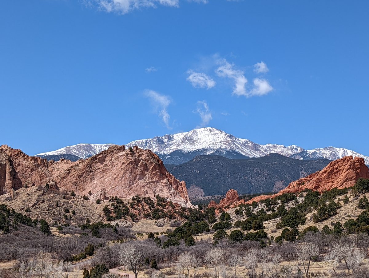 Red sandstone rock formations of Garden of the Gods with snow-capped Pikes Peak rising behind them under a blue sky