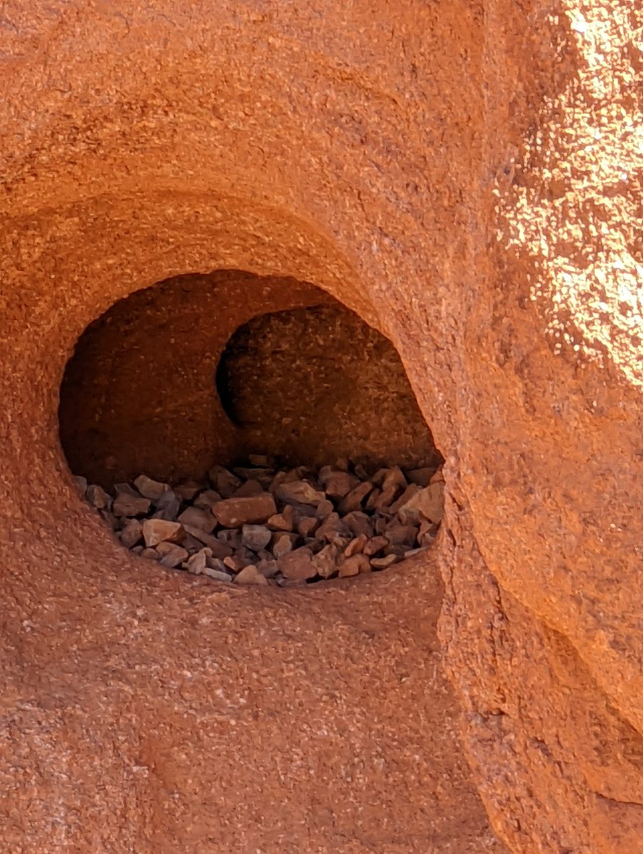 A close-up macro detail of a small weathered hollow in the red sandstone with loose pebbles inside