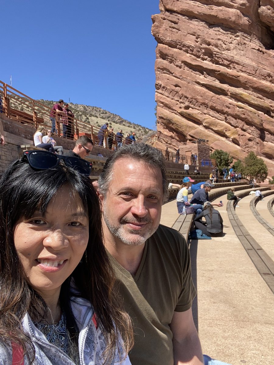 Eddy and Ako smiling together with the Red Rocks amphitheater seating behind them — Colorado 2022