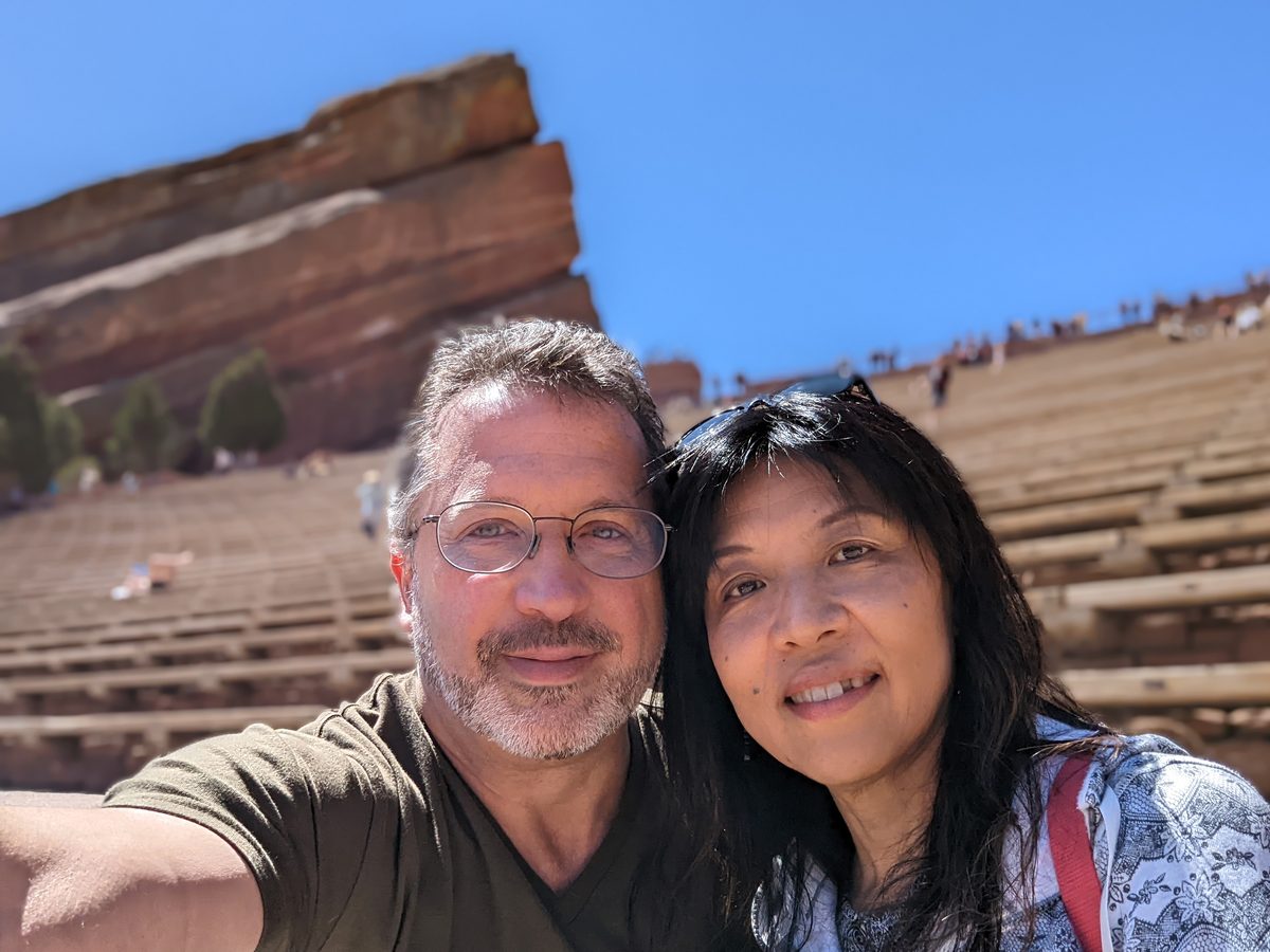 Ako smiling with her arms not raised, standing in front of the rock formation with amphitheater seating behind her