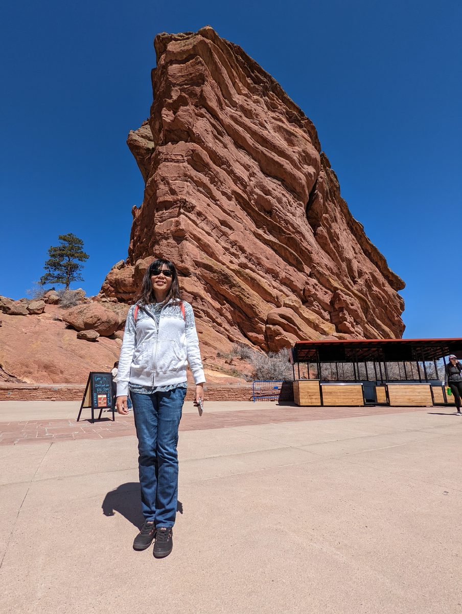 Ako standing in a plaza in front of a towering red rock spire near the visitor center, with informational signage nearby