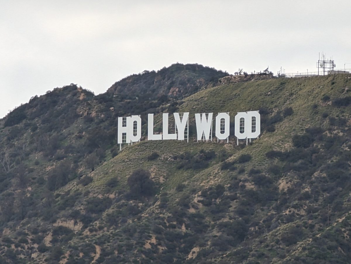 The Hollywood Sign seen from a distance on a green hillside under an overcast sky