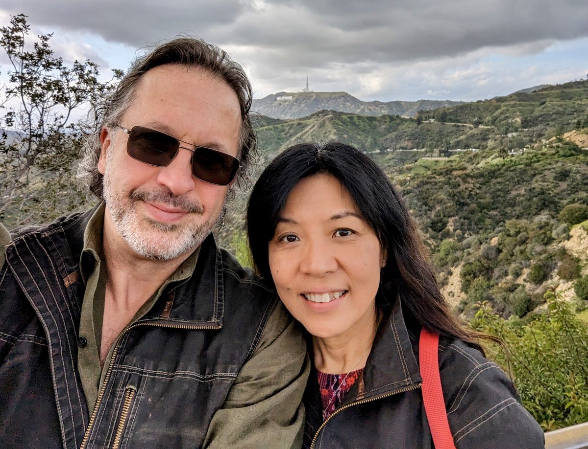 Eddy and Ako smiling together with the Hollywood Sign visible on the hillside behind them — Griffith Park 2023