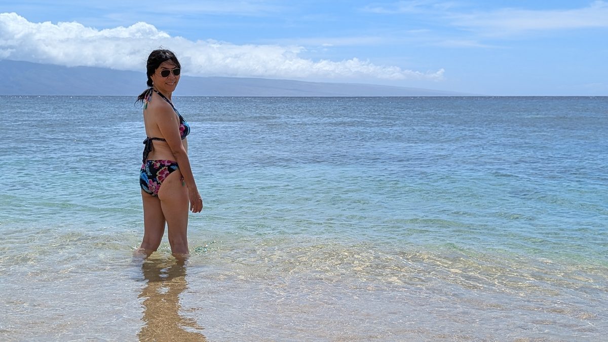 Ako standing in the Ka'anapali shallows, looking back over her shoulder — Molokai and the West Maui Mountains across the channel