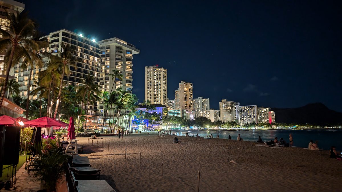 Waikiki beach at night — hotels and restaurants lit up along the waterfront, Diamond Head a dark silhouette in the distance