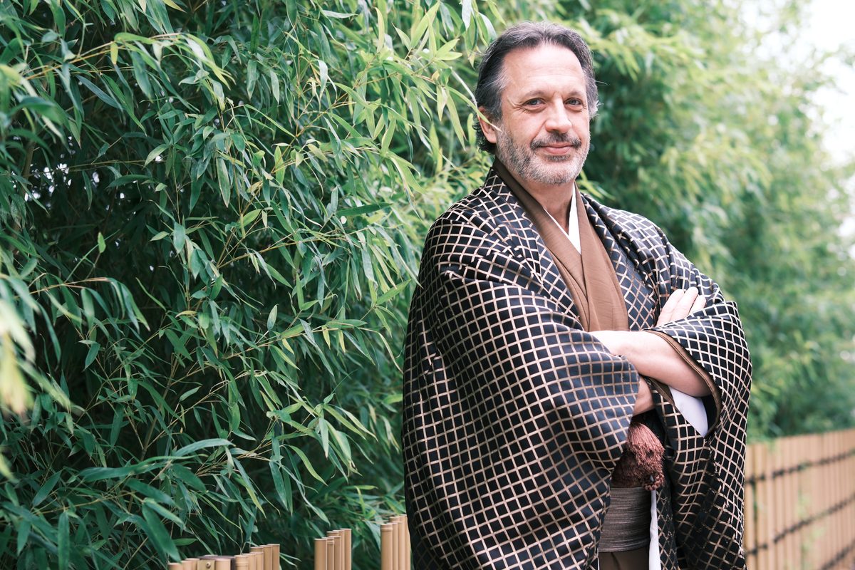 Eddy alone in his black diamond-patterned haori and brown hakama, arms folded in front of bamboo