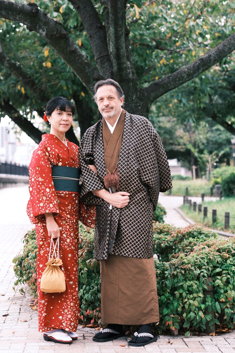 Eddy and Ako walking along a narrow stone-walled lane with ivy and a tall tree, relaxed and laughing