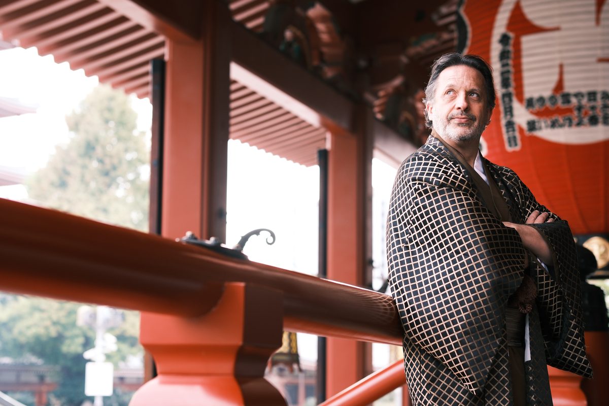 Eddy leaning on the vermilion railing at Sensoji, looking across the temple grounds, red banners behind him