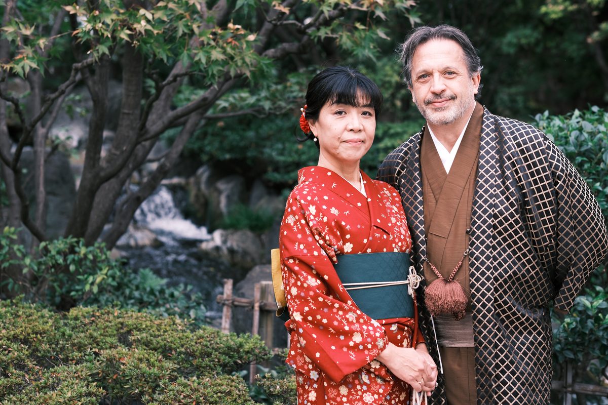 Eddy and Ako in the temple garden, Japanese maple trees in autumn color behind them, a small rock waterfall in the background