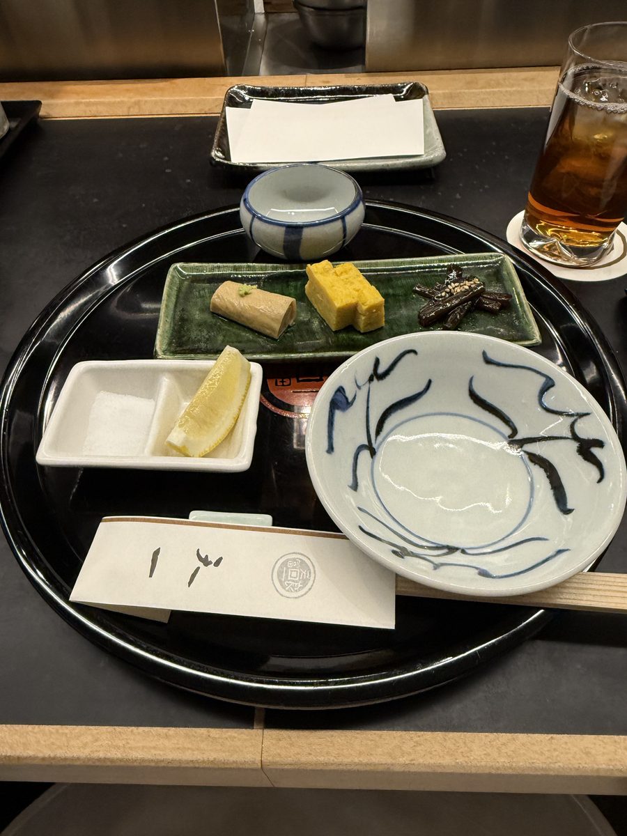 A tempura restaurant tray with tamagoyaki, pickles, and a small ceramic bowl at the counter