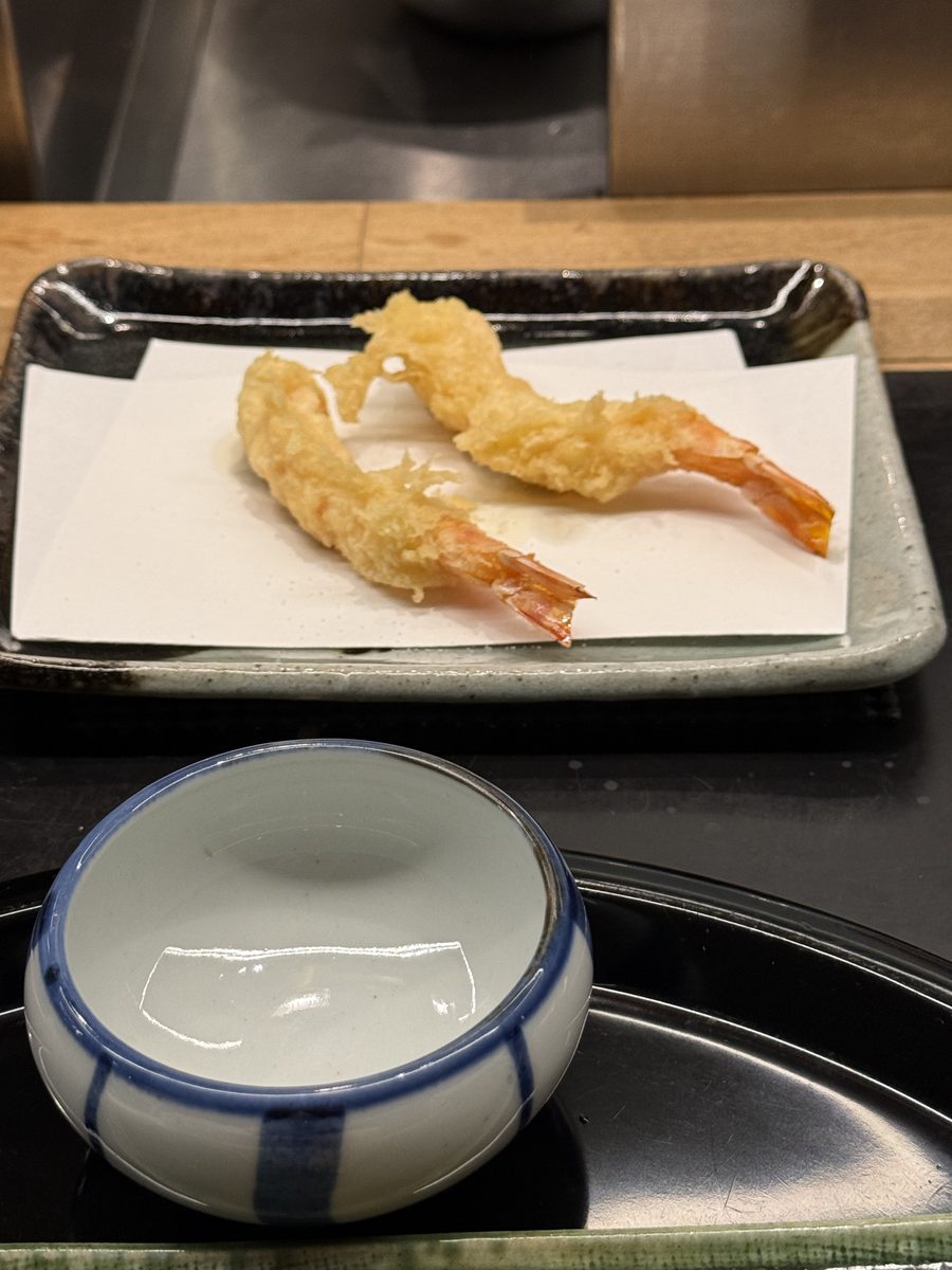 Two pieces of shrimp tempura on a white paper-lined plate