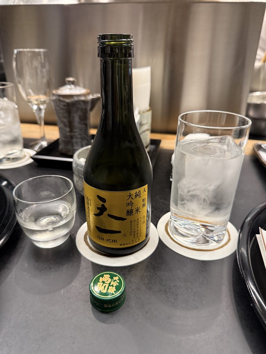 A green glass bottle of Ten-Ichi daiginjo sake on the counter beside glasses of water