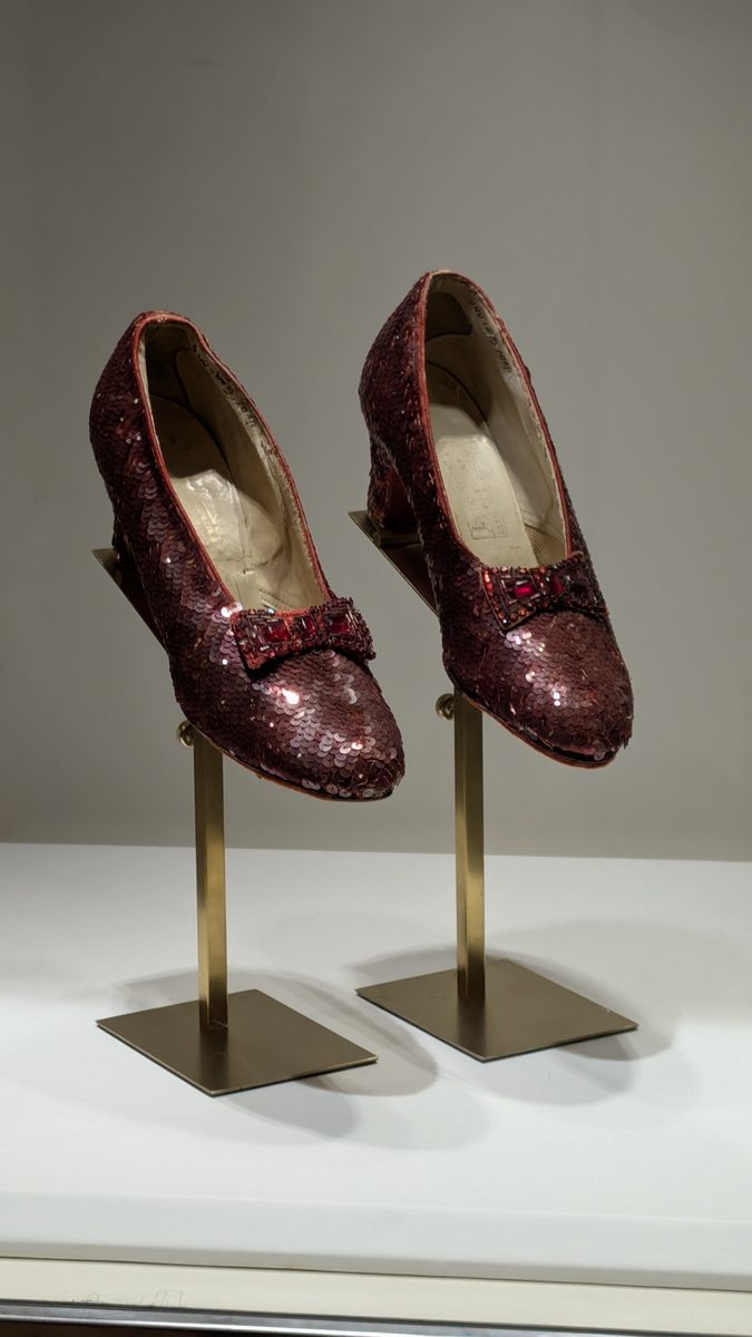 A pair of ruby slippers displayed on stands in a glass museum case