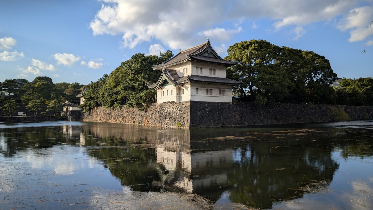 A white-plastered corner watchtower reflected in the palace moat beneath a blue sky
