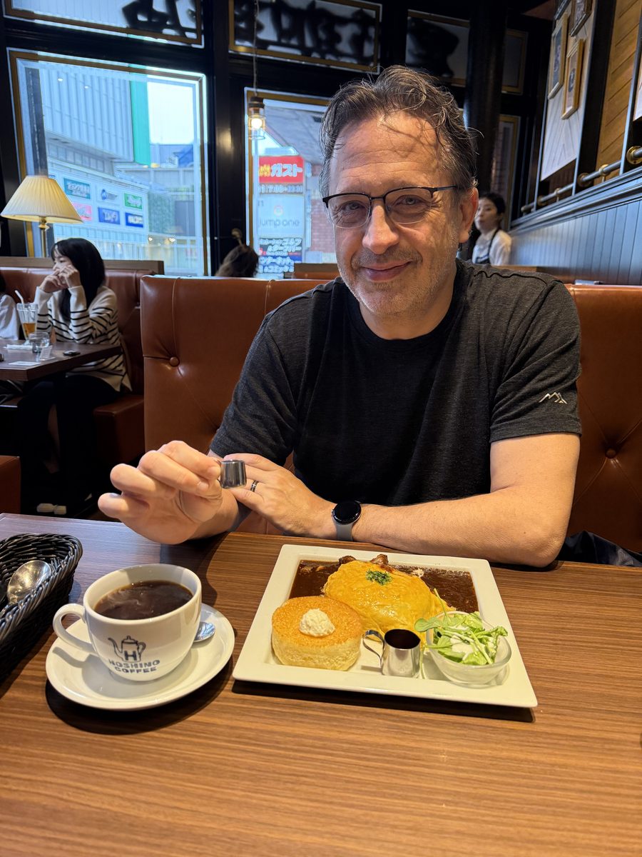 Eddy at a Hoshino Coffee booth with an omurice-curry plate, pancake, and coffee