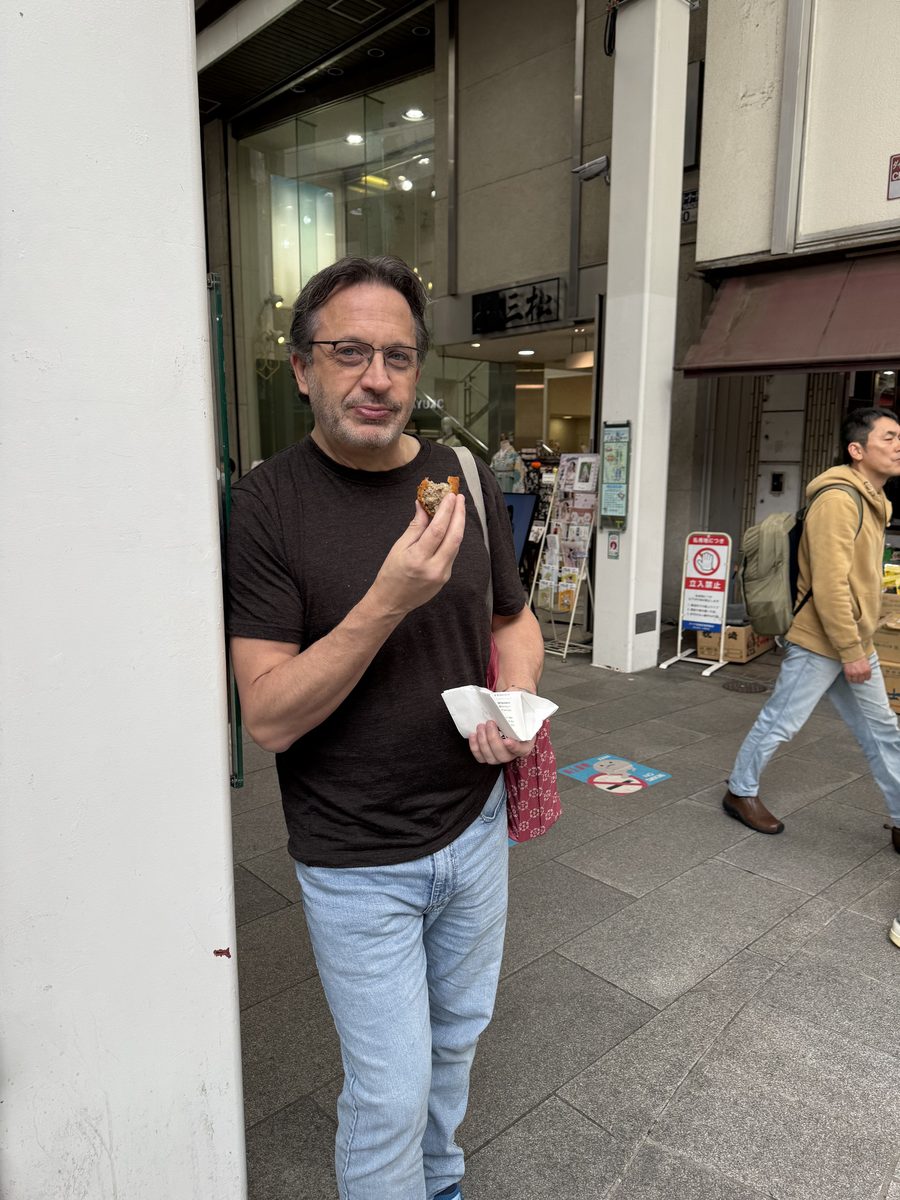 Eddy eating a croquette outside a shopfront on a Kichijoji shopping street