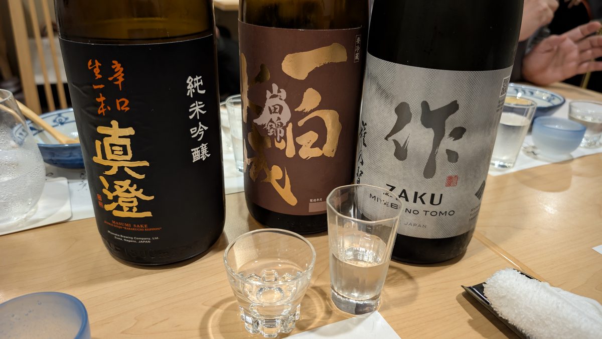 Three bottles of sake with two tasting glasses on an izakaya counter