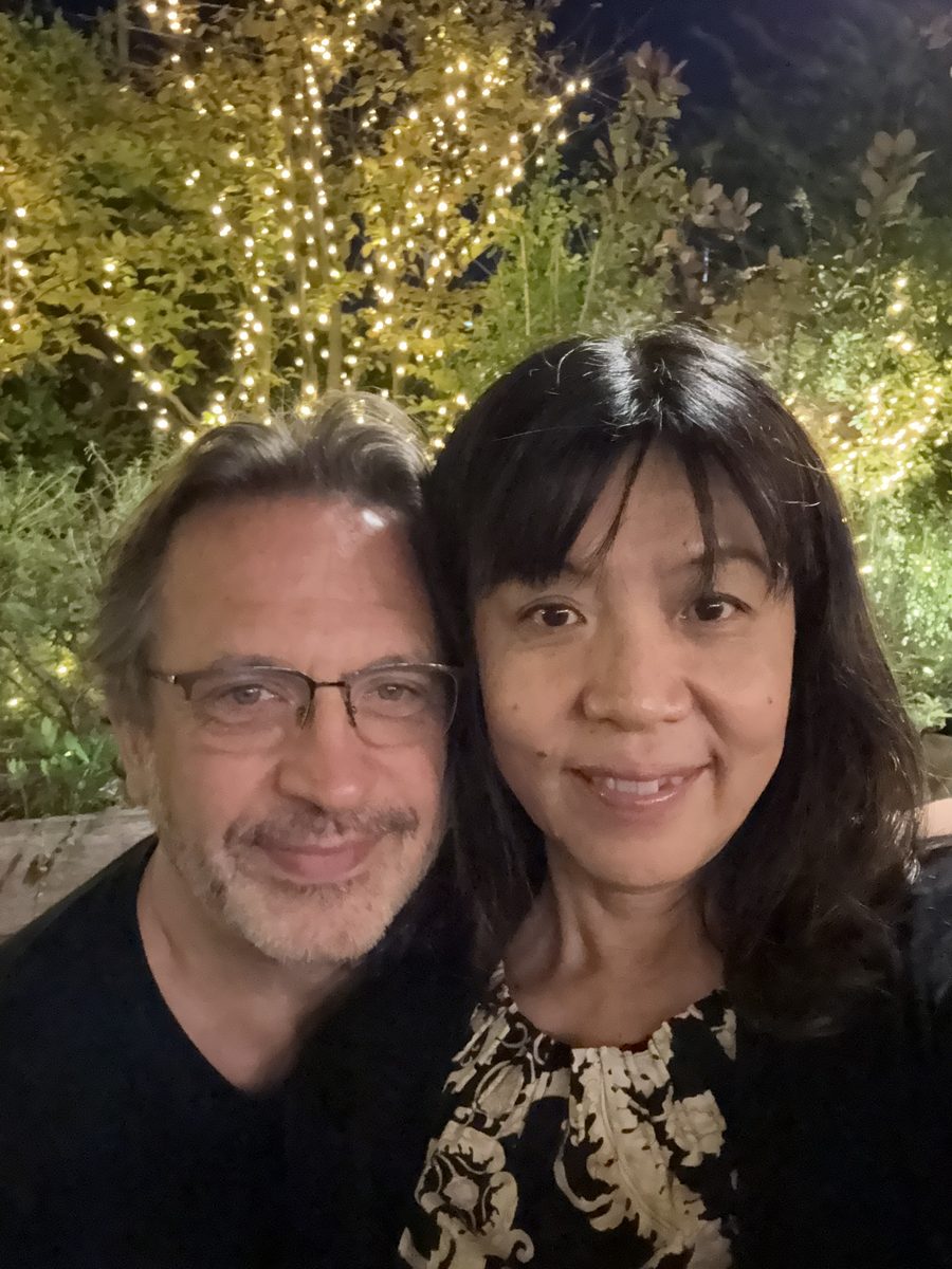 Eddy and Ako in a night selfie under warm string lights at a restaurant