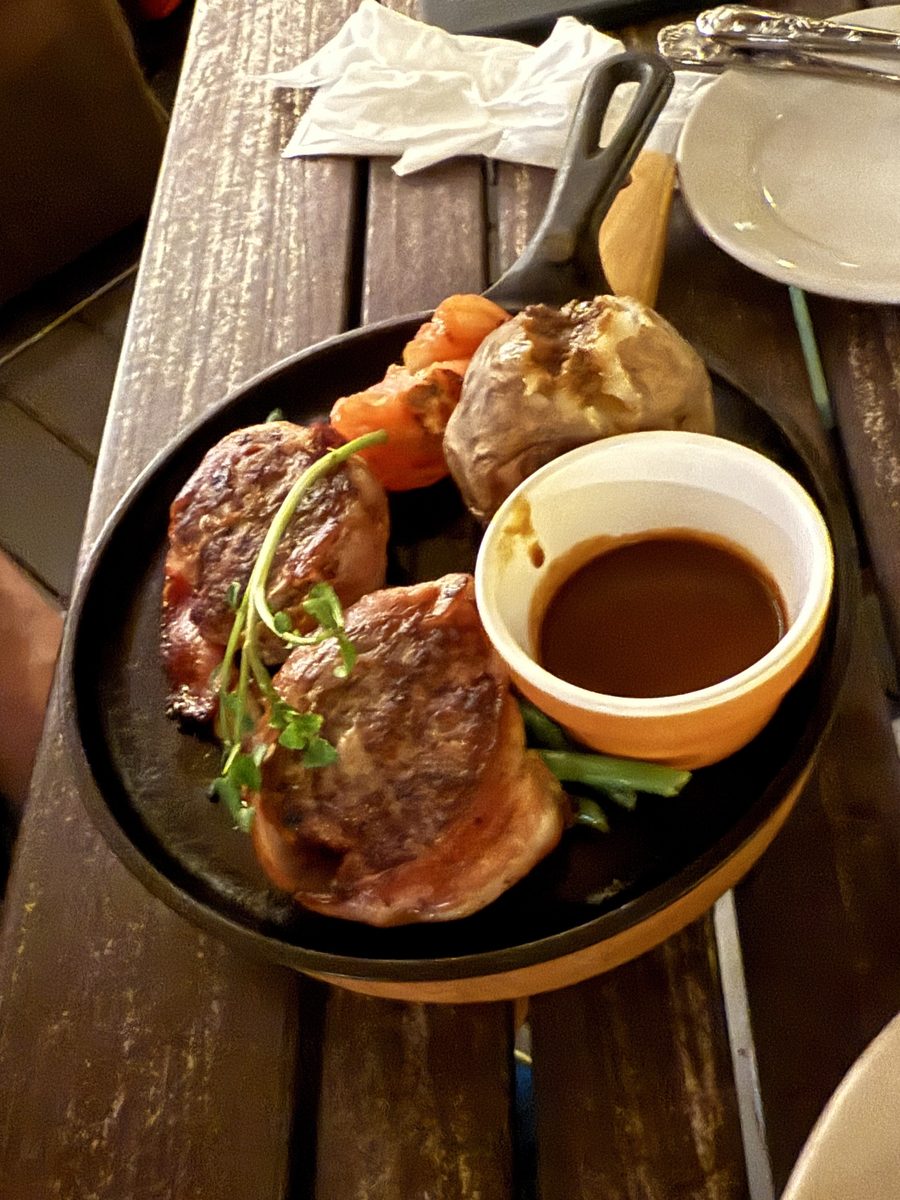 A sizzling iron skillet of bacon-wrapped medallions, baked potato and gravy