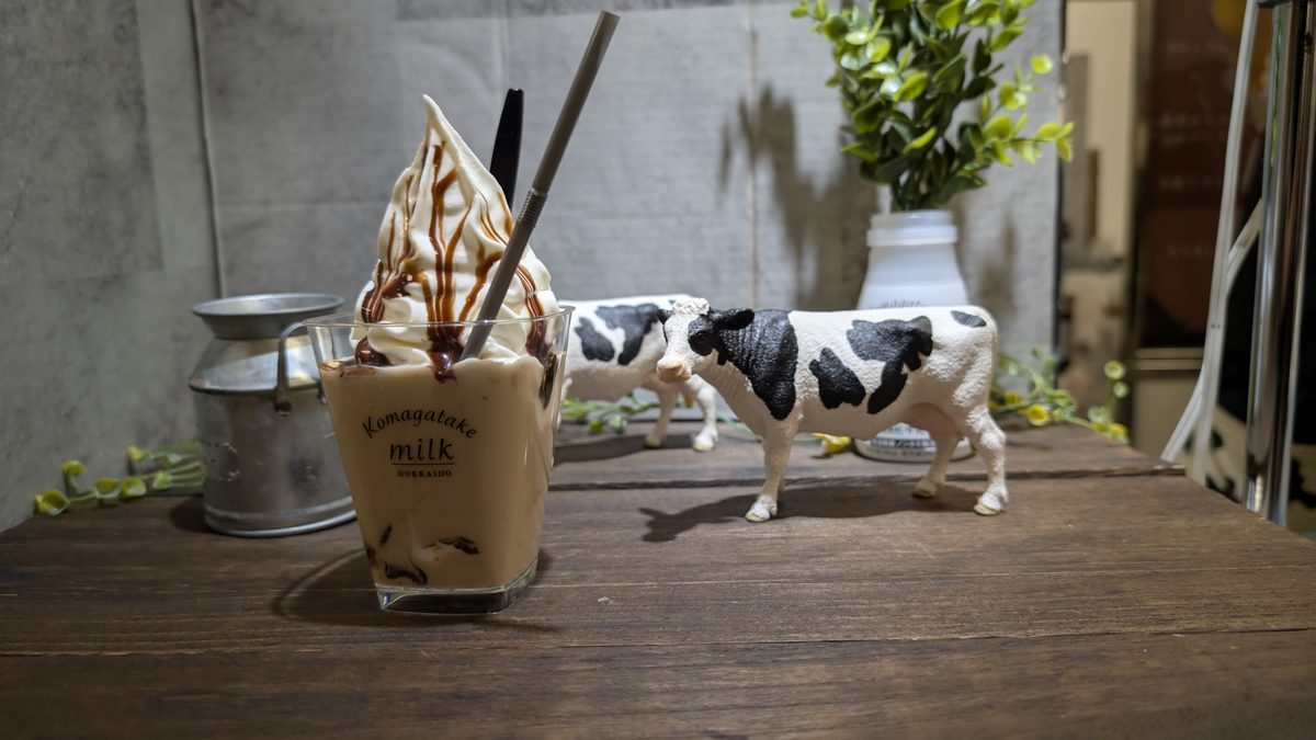 A glass of Hokkaido milk soft-serve float with small toy cows on a wooden table