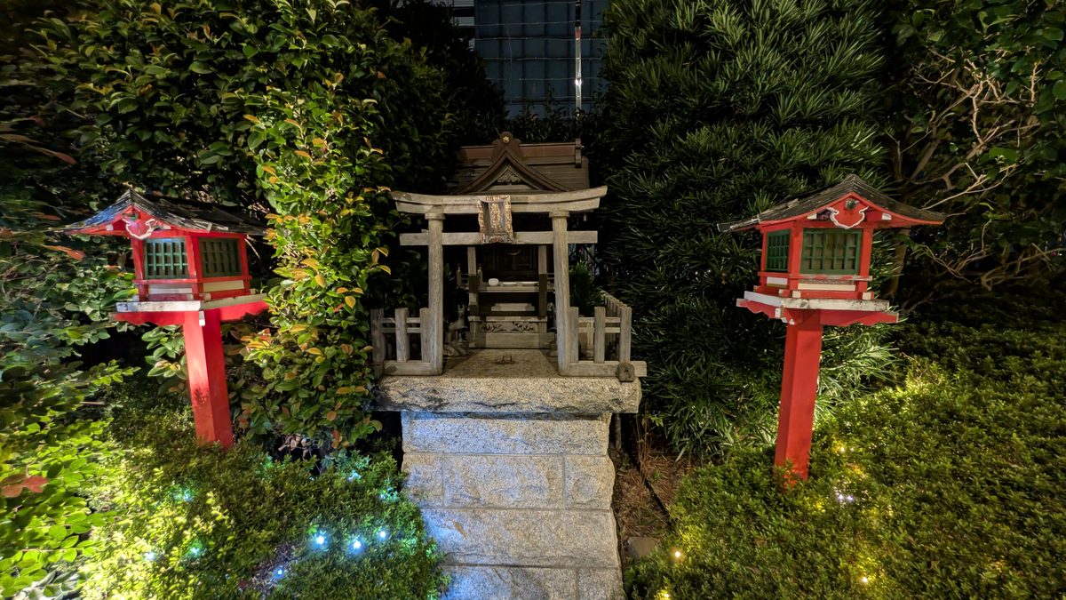 A small Shinto shrine with a stone torii and two red lantern posts lit at night