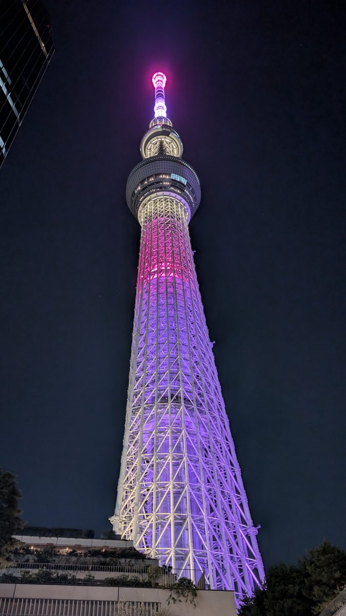 Tokyo Skytree lit purple and pink against the night sky, dramatic upward angle