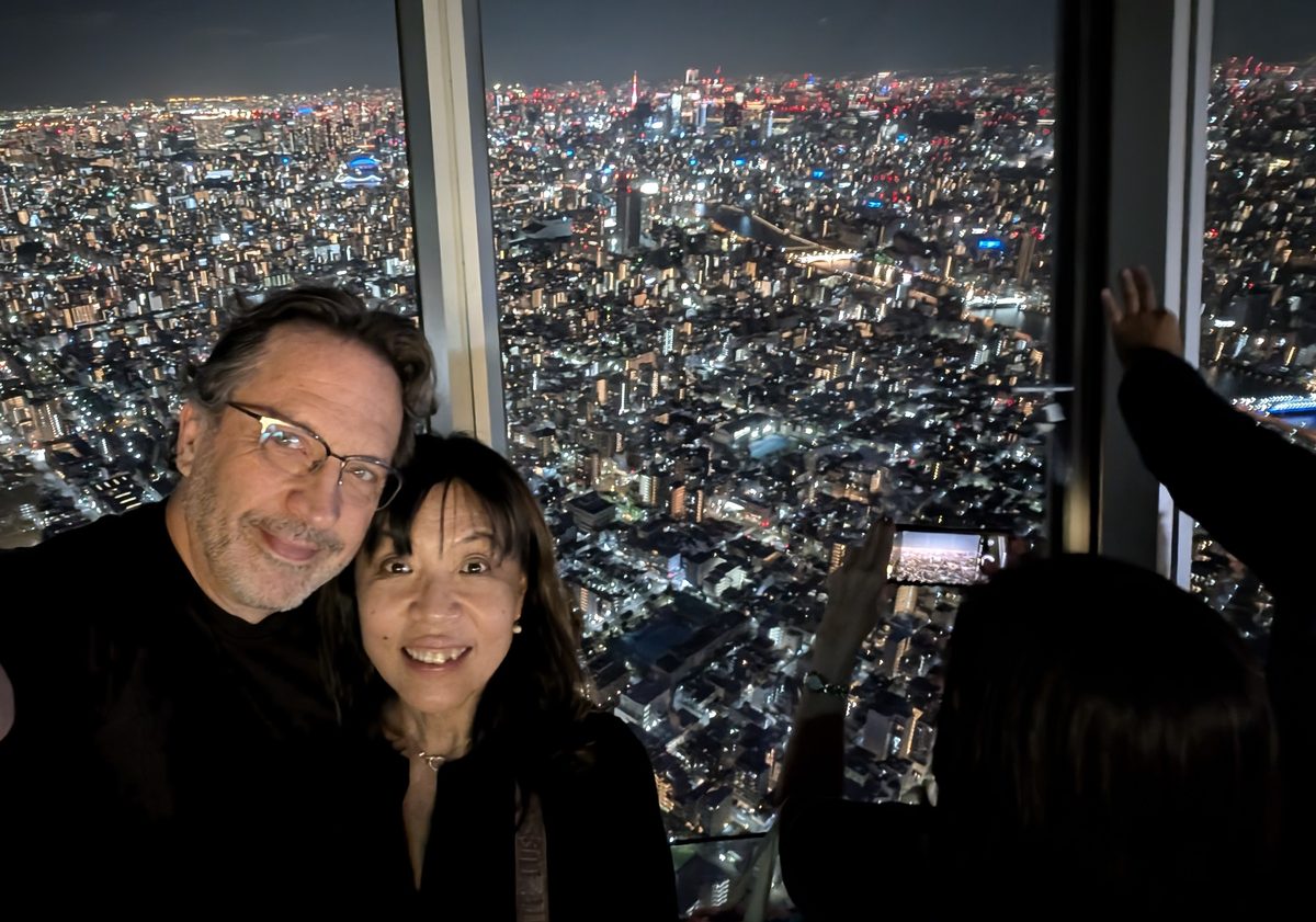 Eddy and Ako in a selfie on the Skytree observation deck, the vast night city behind the glass