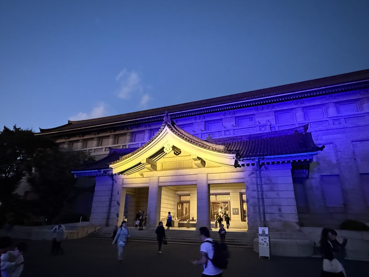 The floodlit main building of the Tokyo National Museum at dusk, its curved tiled roof lit gold and blue