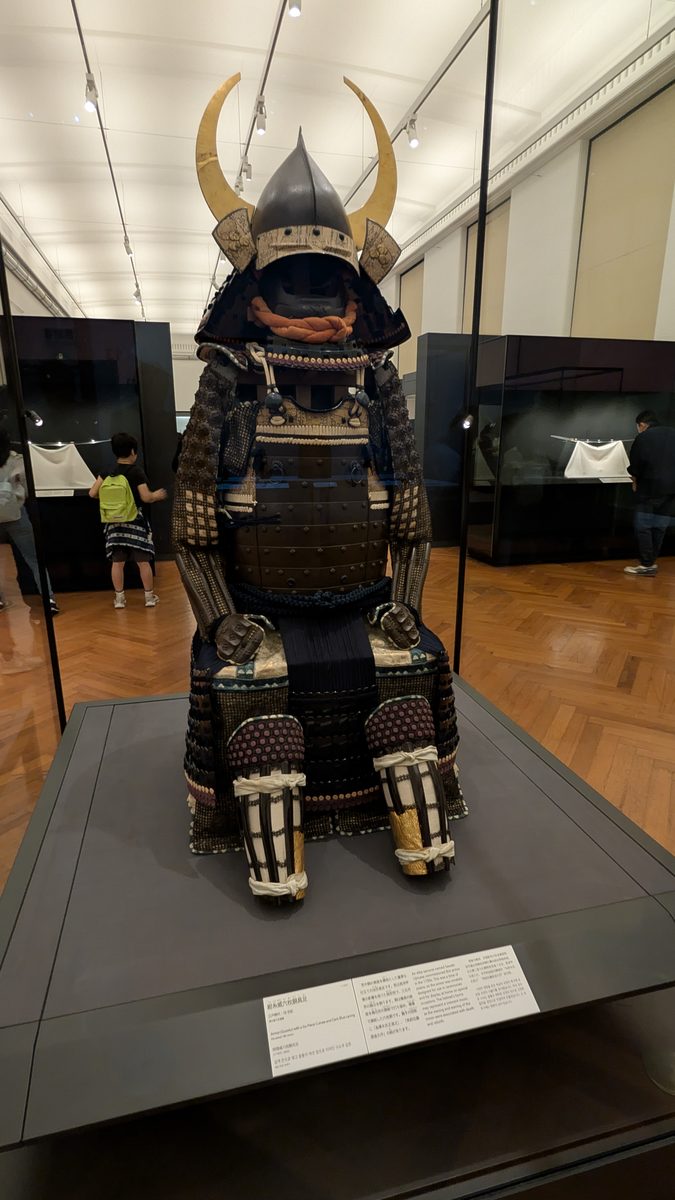 A suit of samurai armor with a horned helmet displayed in a glass case