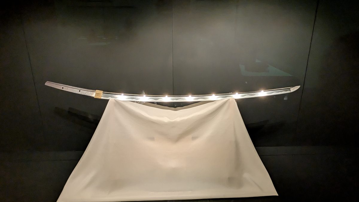 A single curved Japanese tachi sword blade displayed on a white cloth mount
