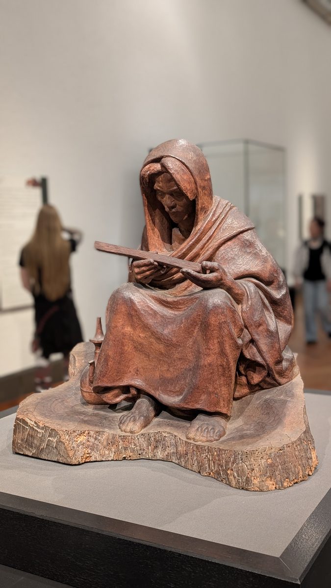 A carved wooden sculpture of a seated hooded monk holding a tablet