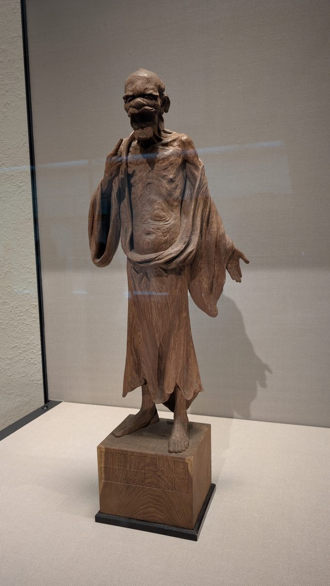 A gaunt standing wooden statue of an emaciated ascetic figure