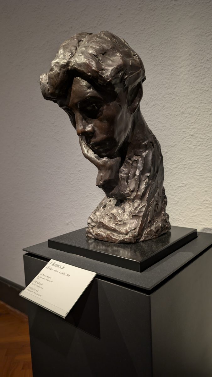 A modern bronze bust of a head resting on a hand, on a pedestal
