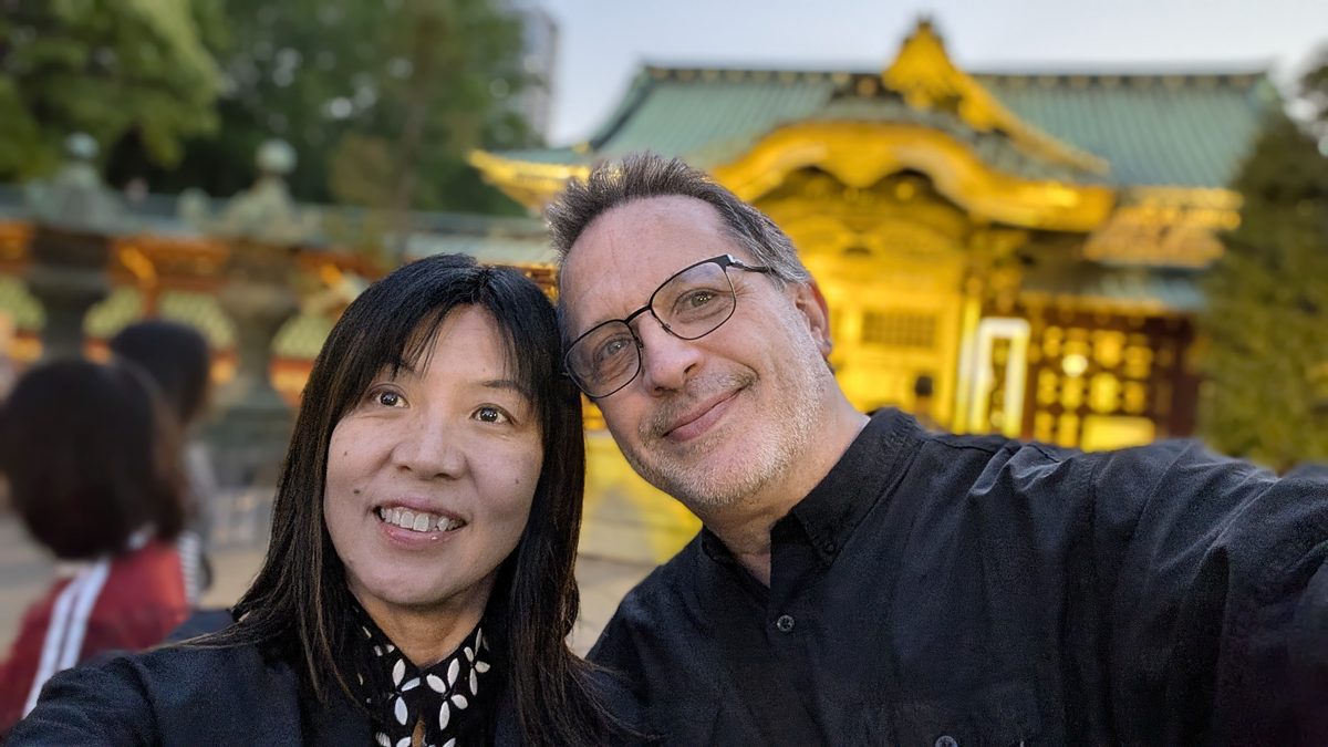 Eddy and Ako in a dusk selfie with the golden Ueno Tōshōgū shrine glowing behind them — Japan 2026