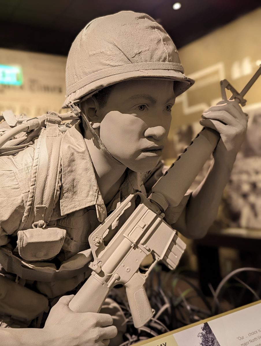 A life-size grey sculpture of a Vietnam War soldier with helmet, rifle and radio handset