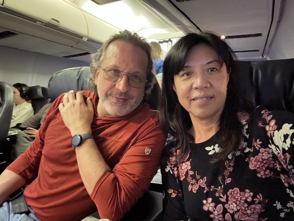 Eddy resting his head on Ako's shoulder, both content in their first-class seats on the flight home