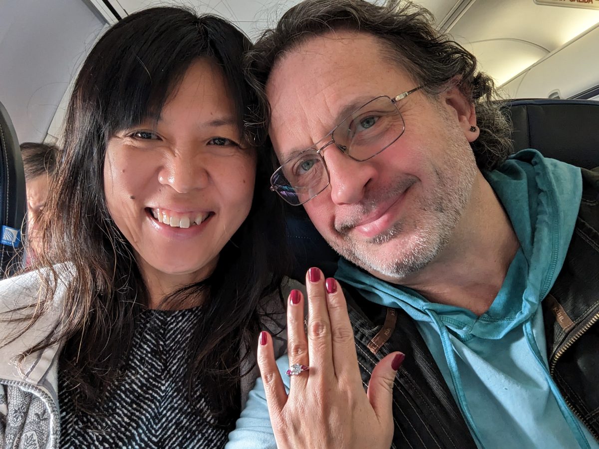 Ako holding up her hand with the engagement ring on the plane to Tampa, Eddy beside her — Tampa 2023