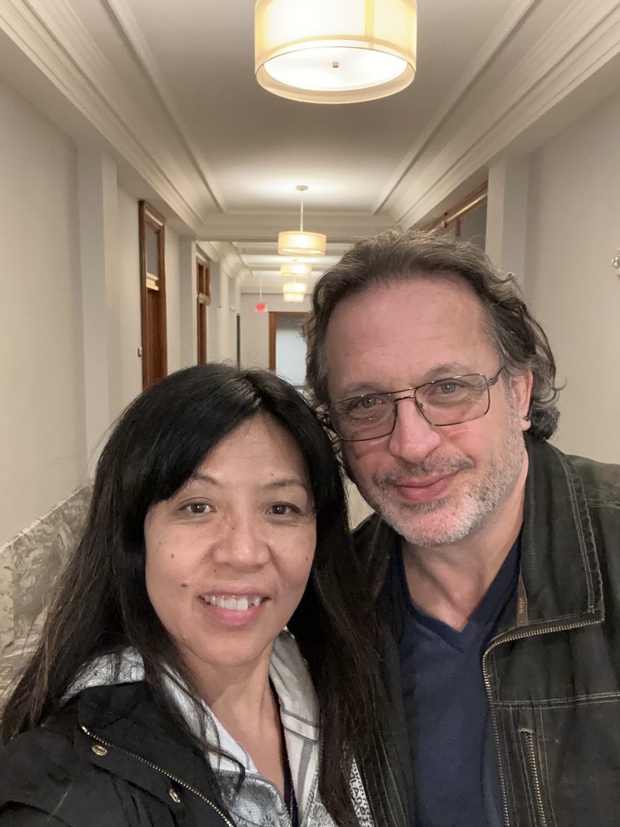 Eddy and Ako in a close selfie in an elegant warmly-lit hotel hallway